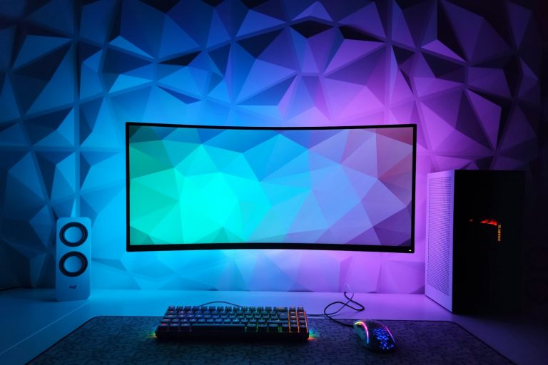 A curved monitor on a desk in a room lit with colored lights