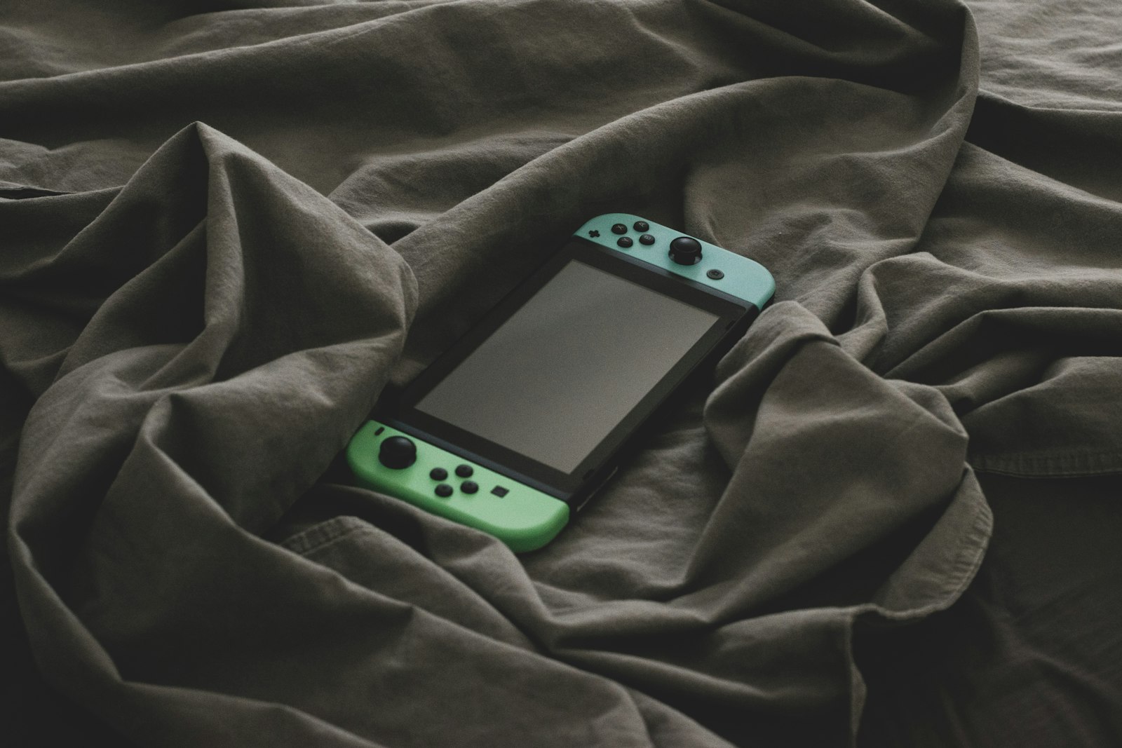 A handheld game console lying on a rumpled bedsheet